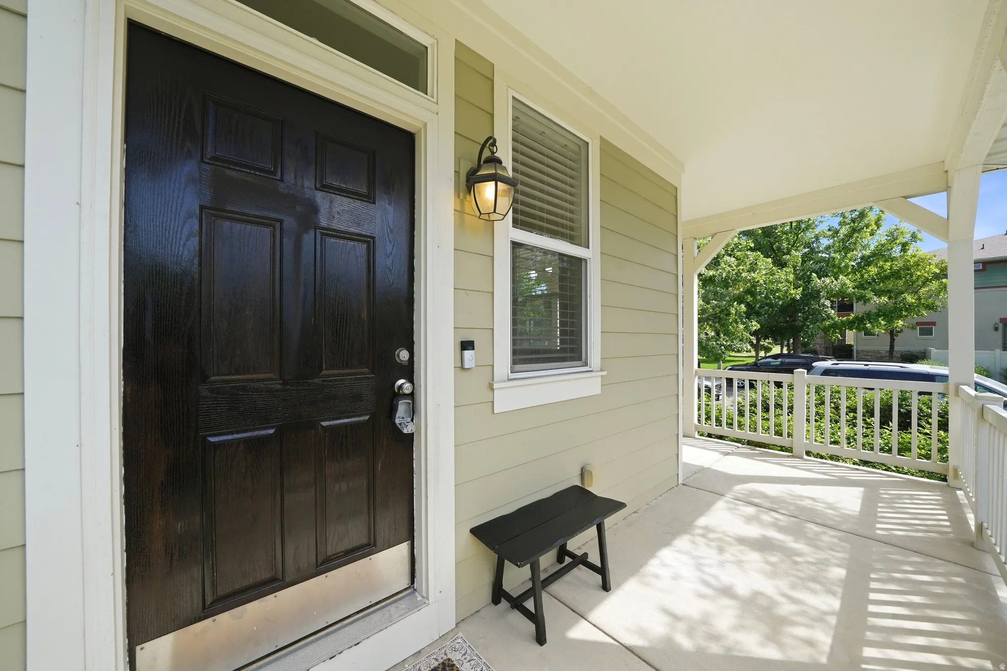 Covered porch with concrete flooring, showcasing a paneled entry door with transom window and exterior lighting