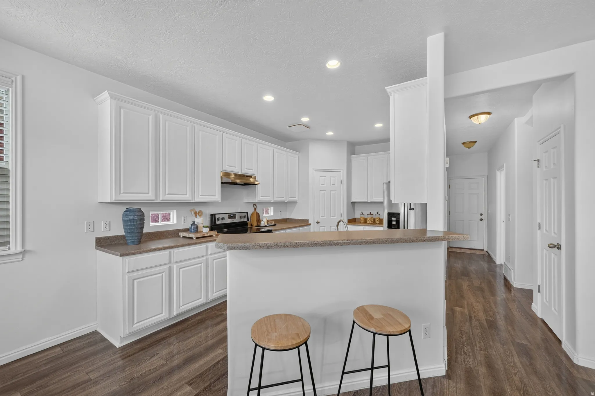 Kitchen featuring white cabinetry, light countertops, wood-finish flooring, recessed lighting, and a breakfast bar