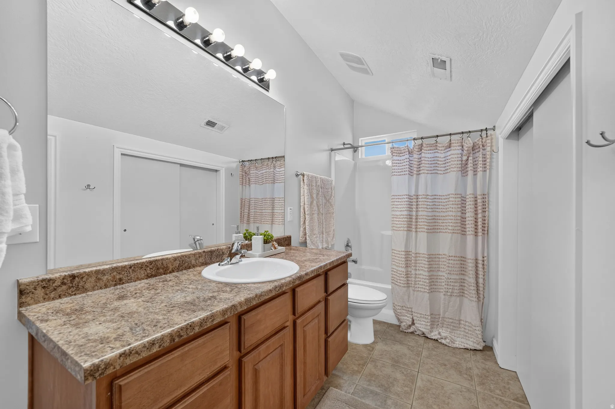 Bathroom featuring an elongated vanity with a single sink, wood cabinetry, and a spacious mirror with a vanity light bar