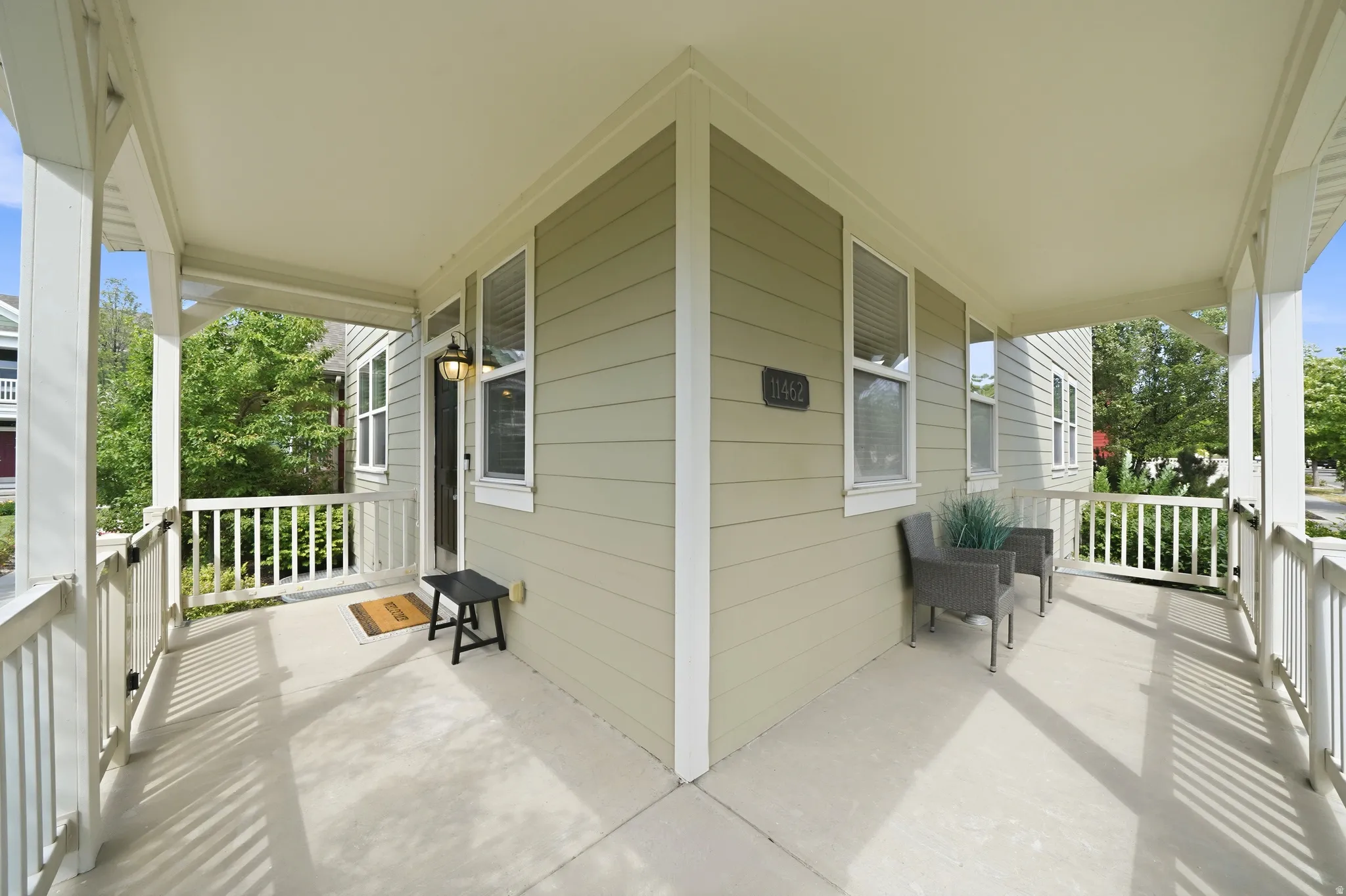 Expansive wrap-around porch featuring a light-colored concrete surface, white railing, and a light green exterior with white trim