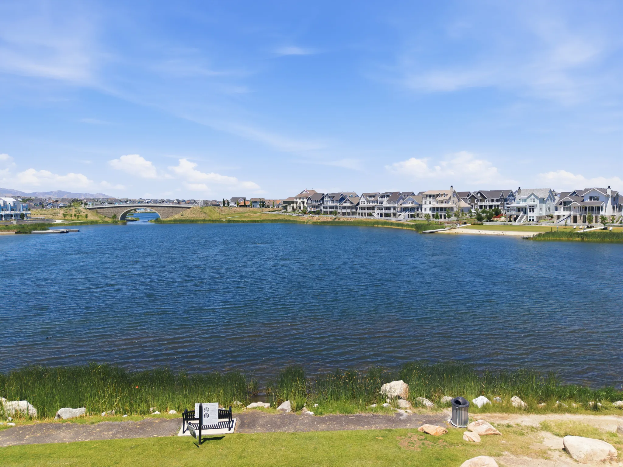 Expansive waterfront property featuring a large lake with sandy shores, a stone bridge, and a collection of multi-story homes