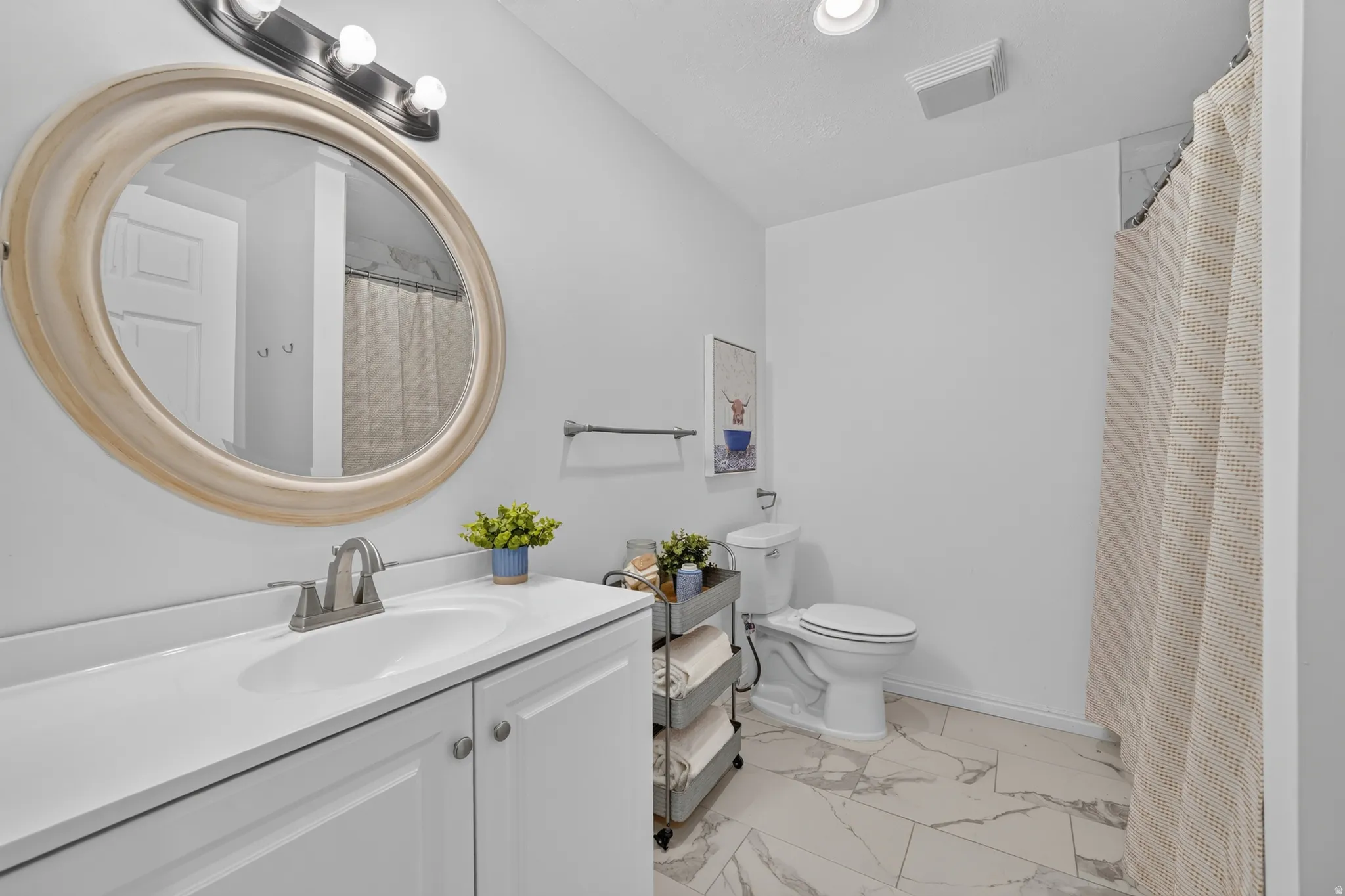 Bathroom featuring a single vanity with an integrated sink, brushed nickel faucet, and a large round mirror