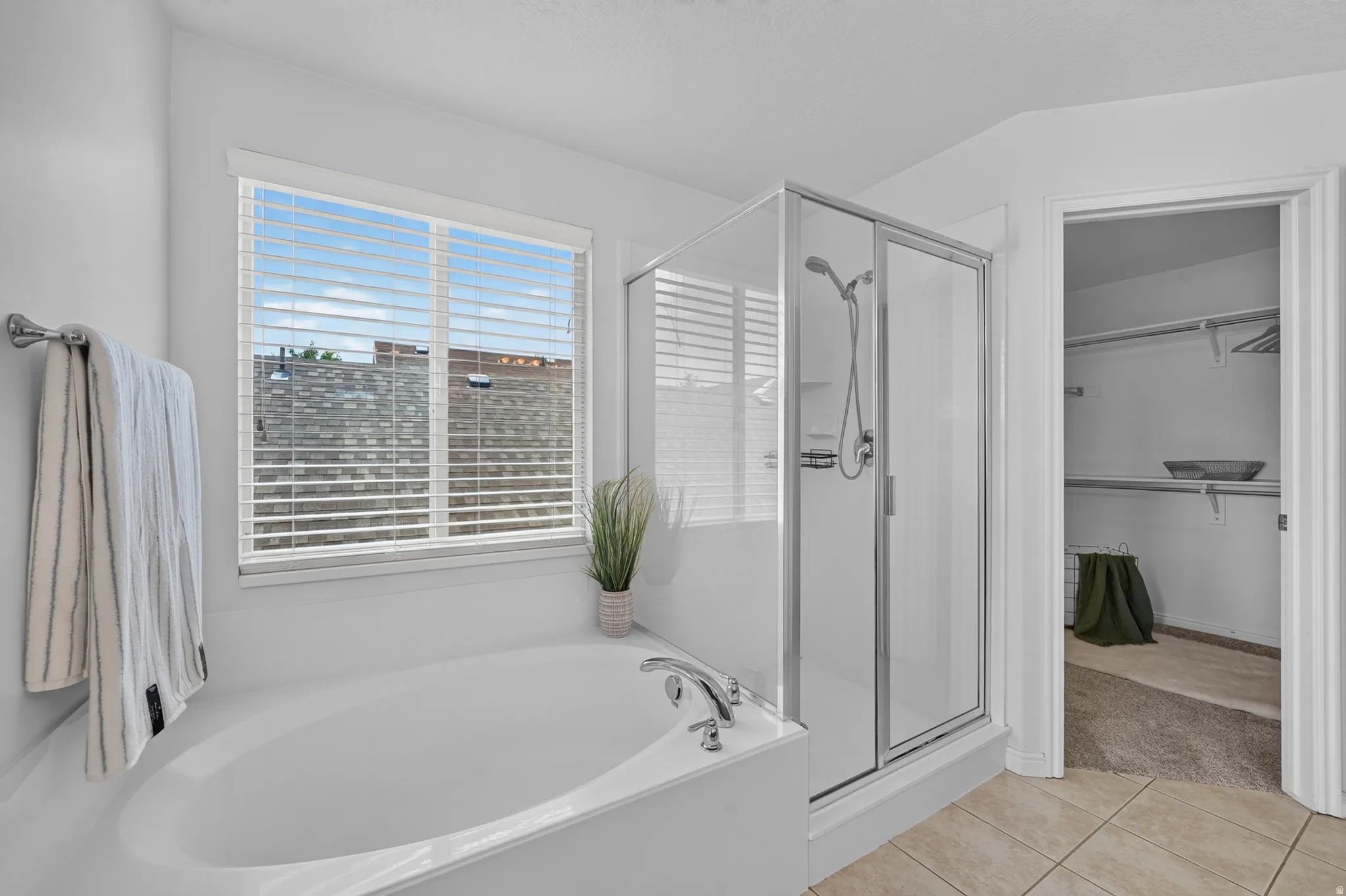 Bathroom featuring a built-in soaking tub, an enclosed glass shower, and a window with blinds