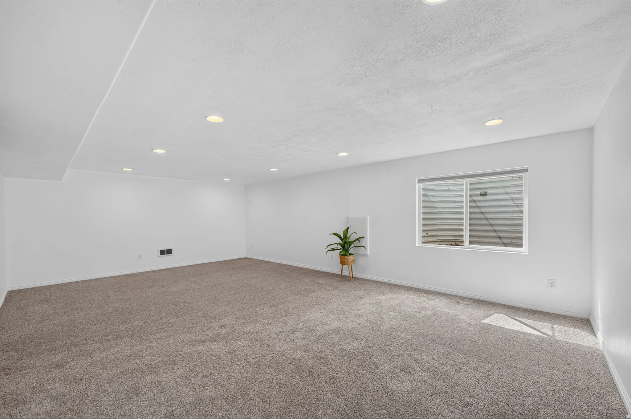 Spacious room featuring neutral carpeting, recessed lighting, and a single window with a white frame