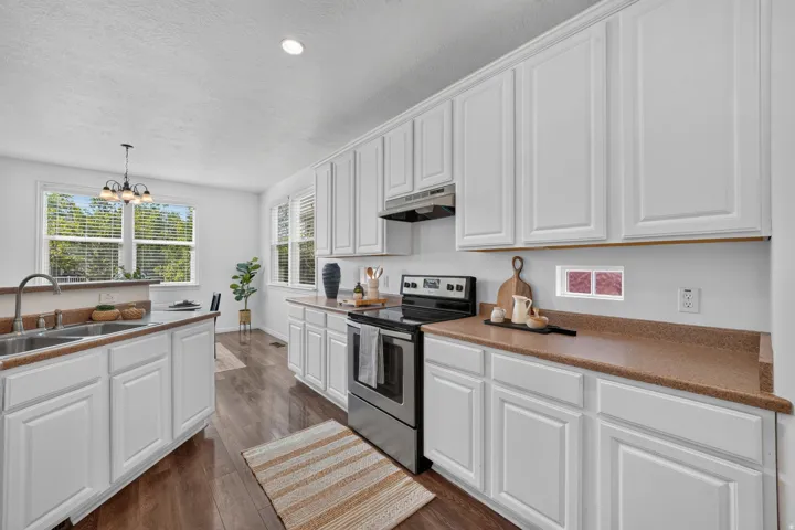 Bright kitchen featuring extensive white cabinetry, durable laminate countertops, stainless steel appliances, wood-finish flooring, and ample natural light from multiple windows
