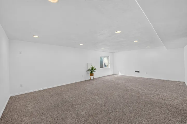 Spacious room featuring neutral carpeting, white walls, recessed lighting, and a window with horizontal blinds