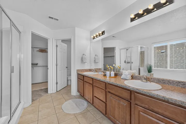 Dual vanity with wood-finish cabinetry, speckled countertop, and integrated sinks