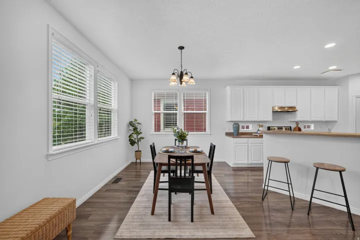 Open-concept dining area featuring wood-finish flooring, multiple windows with blinds, and a chandelier