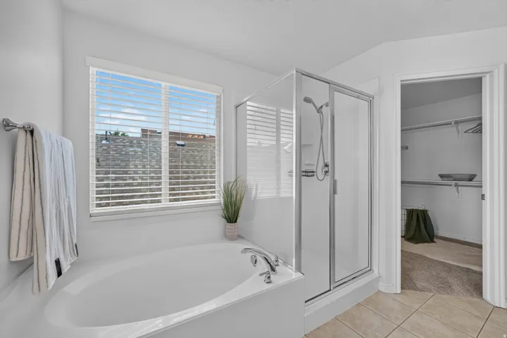 Bathroom featuring a built-in soaking tub, an enclosed glass shower, and a window with blinds