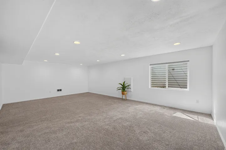 Spacious room featuring neutral carpeting, recessed lighting, and a single window with a white frame