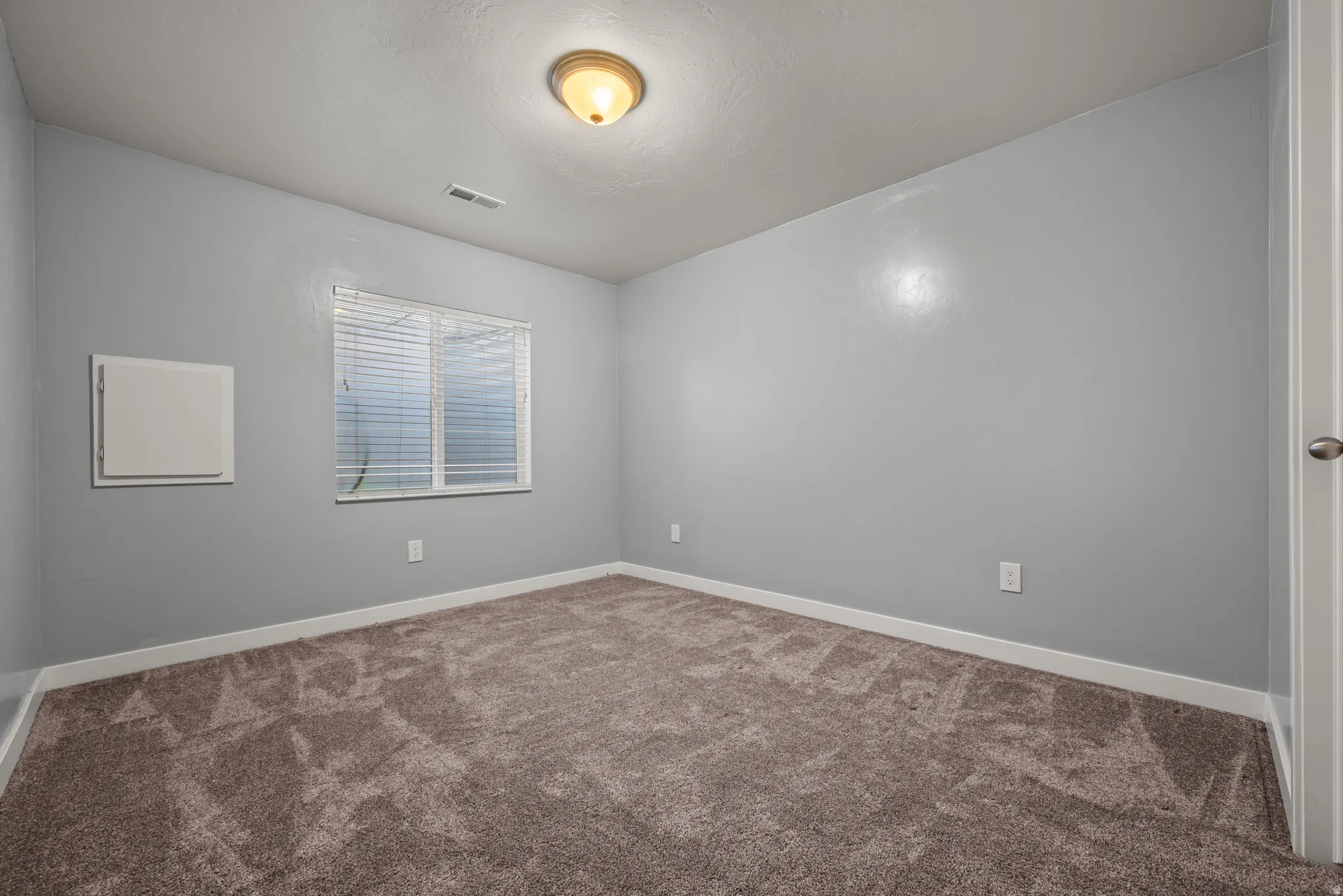 Carpeted room featuring light gray walls, white baseboards, and a single window with horizontal blinds