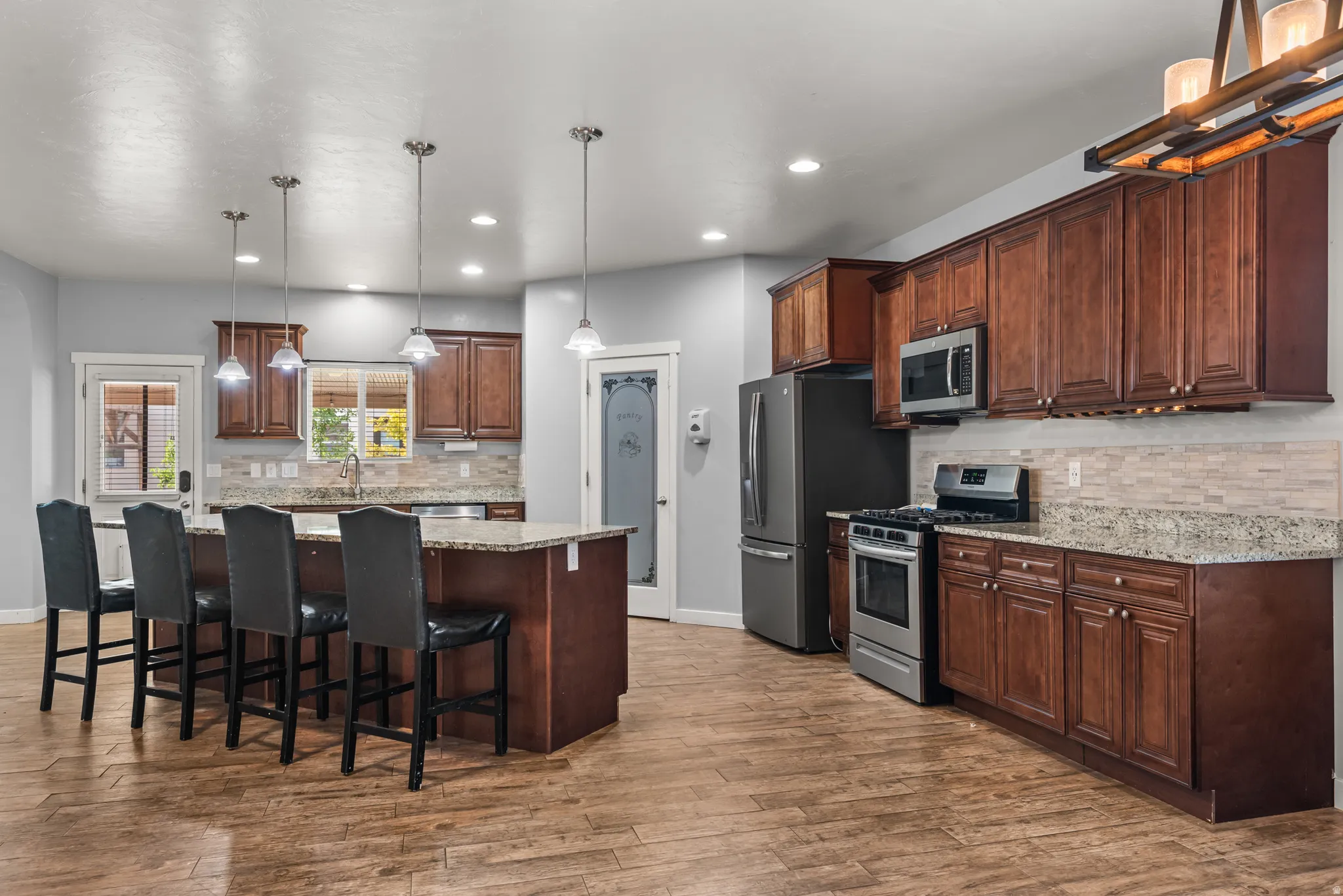 Kitchen featuring a central island with bar seating, granite countertops, wood-finish flooring, stainless steel appliances, and abundant wood cabinetry
