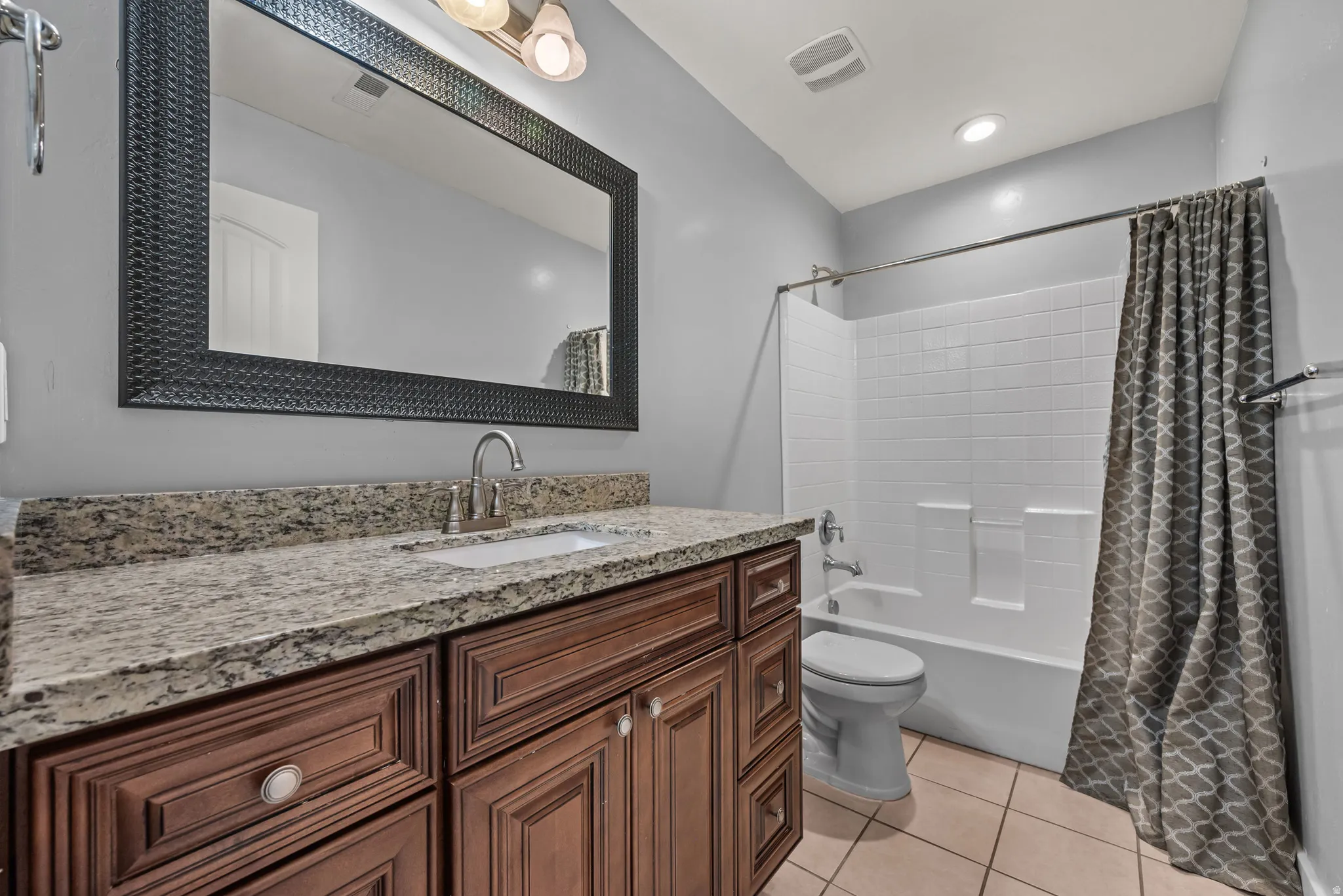 Bathroom featuring a rich wood-tone vanity with a light granite countertop, an undermount sink, and a framed mirror