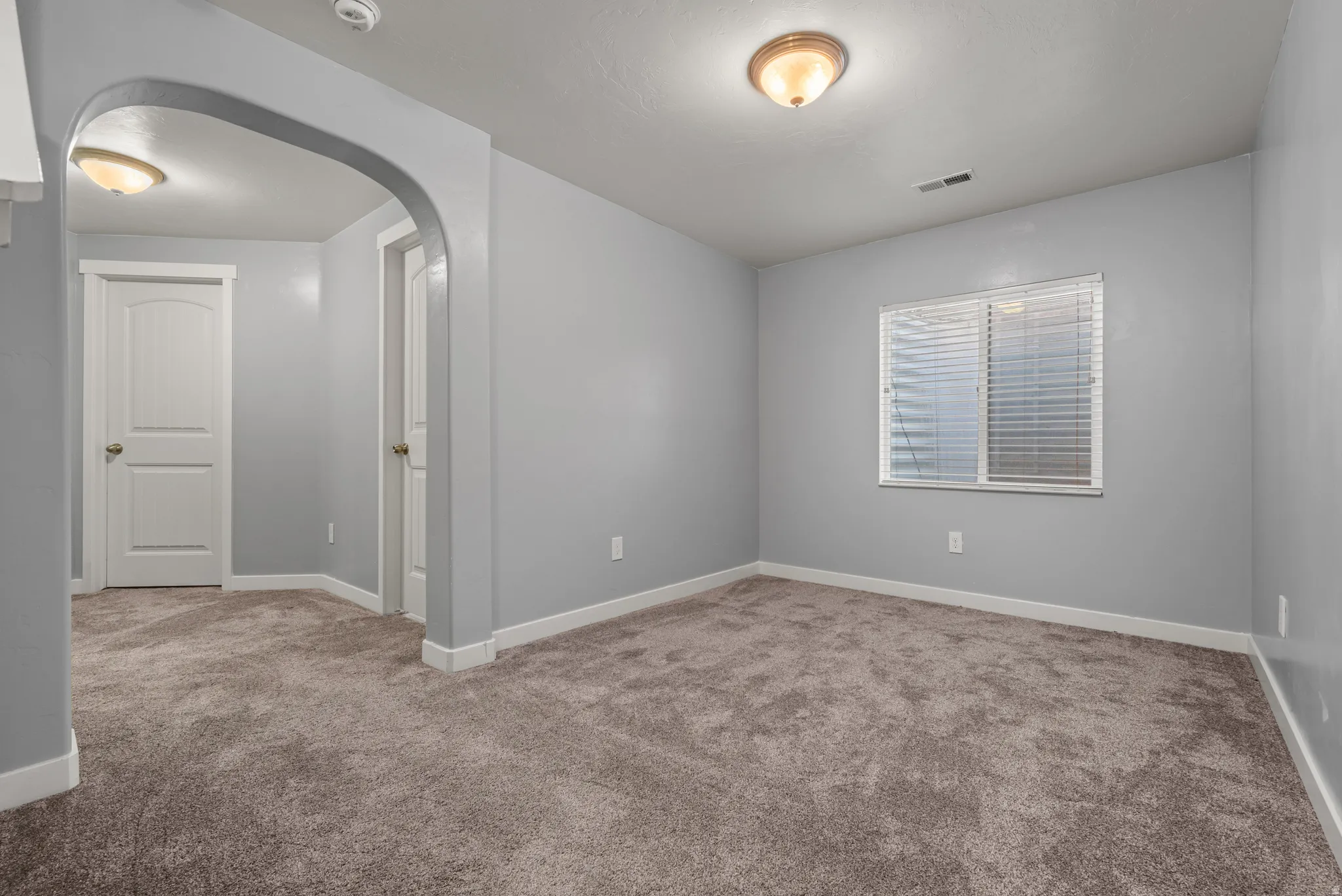 Carpeted interior space with light grey walls, white baseboards, and a window with blinds