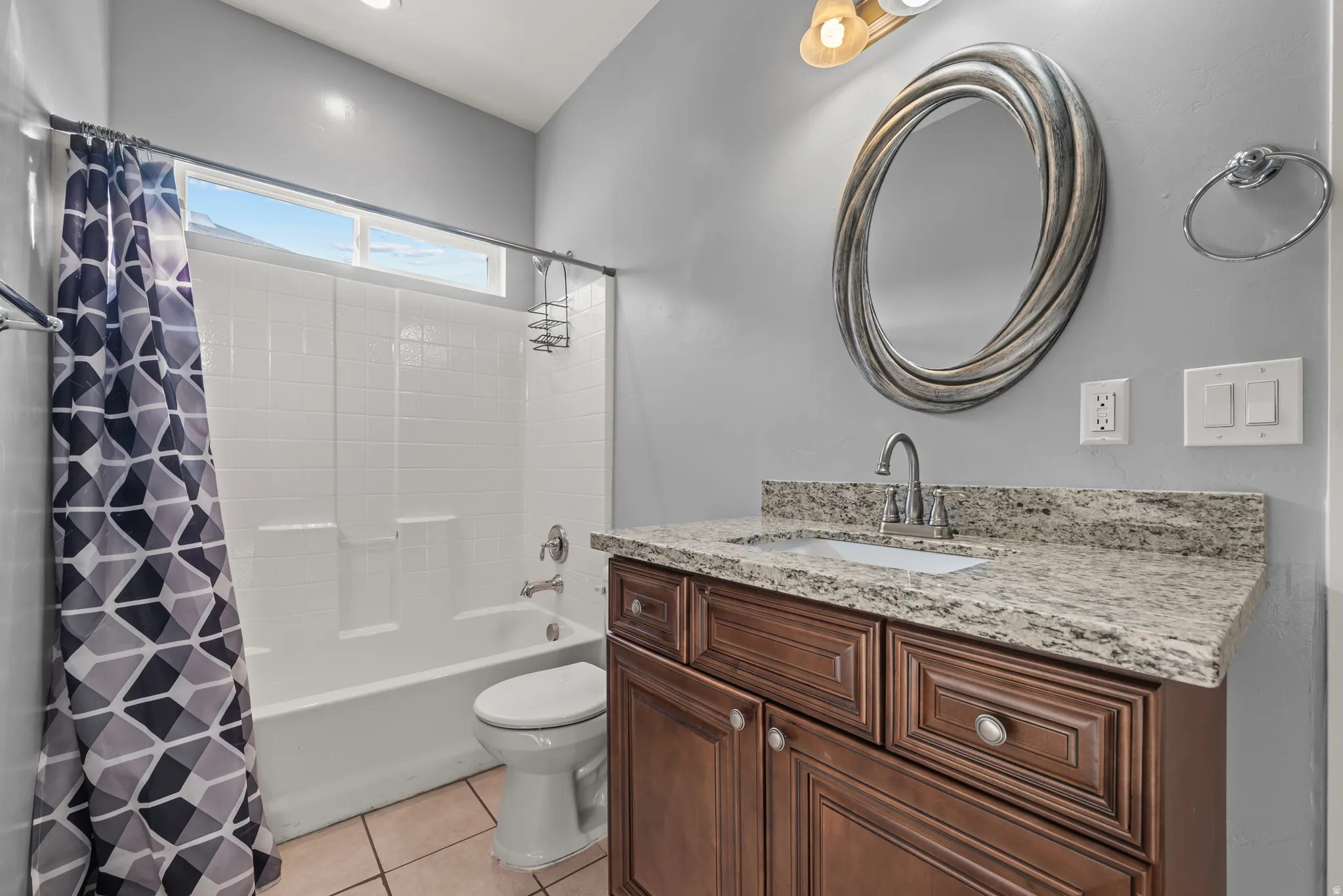 Bathroom featuring a wood-finish vanity with a light-toned countertop, an oval-shaped mirror, and a built-in tub with white subway tile surround