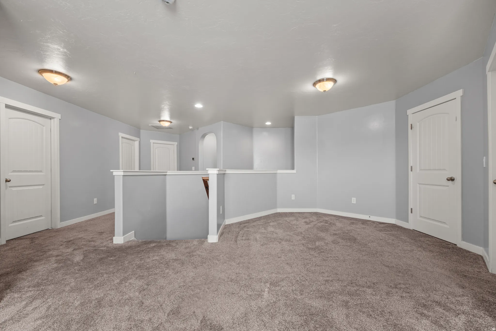 Spacious carpeted landing area with light gray walls, white trim, multiple paneled doors, and recessed lighting