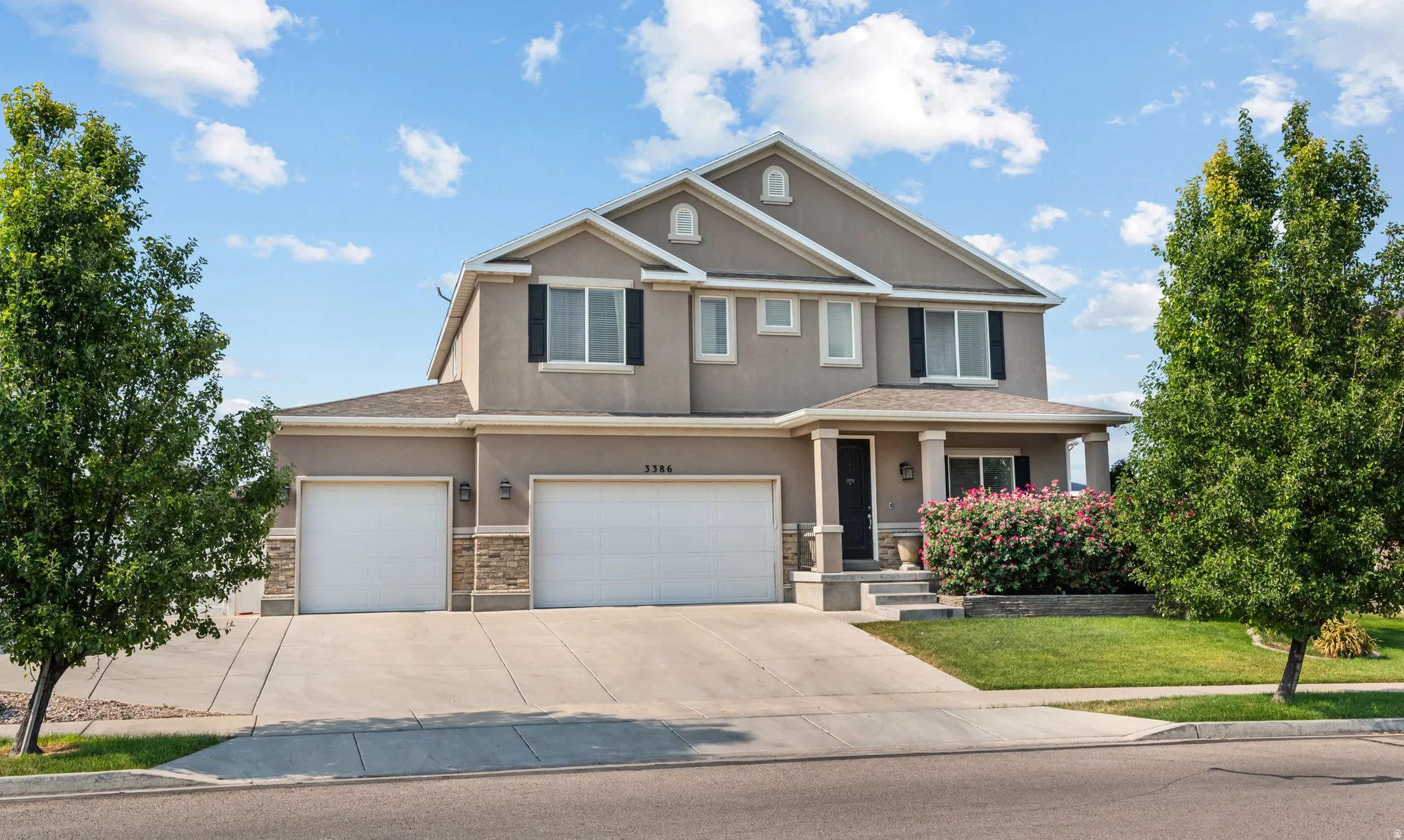 Two-story stucco residence featuring a covered front porch, dual garage doors, and stone facade accents