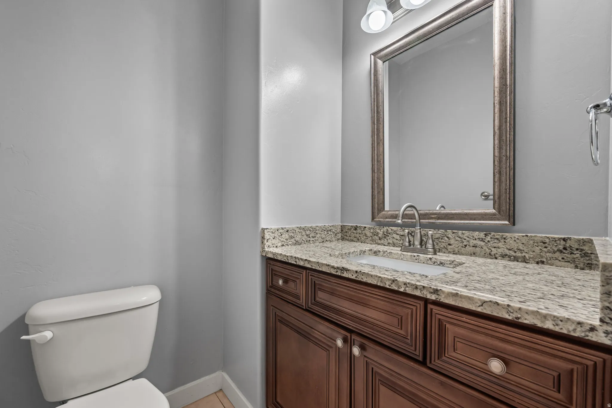 Bathroom vanity featuring a light-toned granite countertop, undermount sink, and dark wood-finish cabinetry with silver-tone hardware