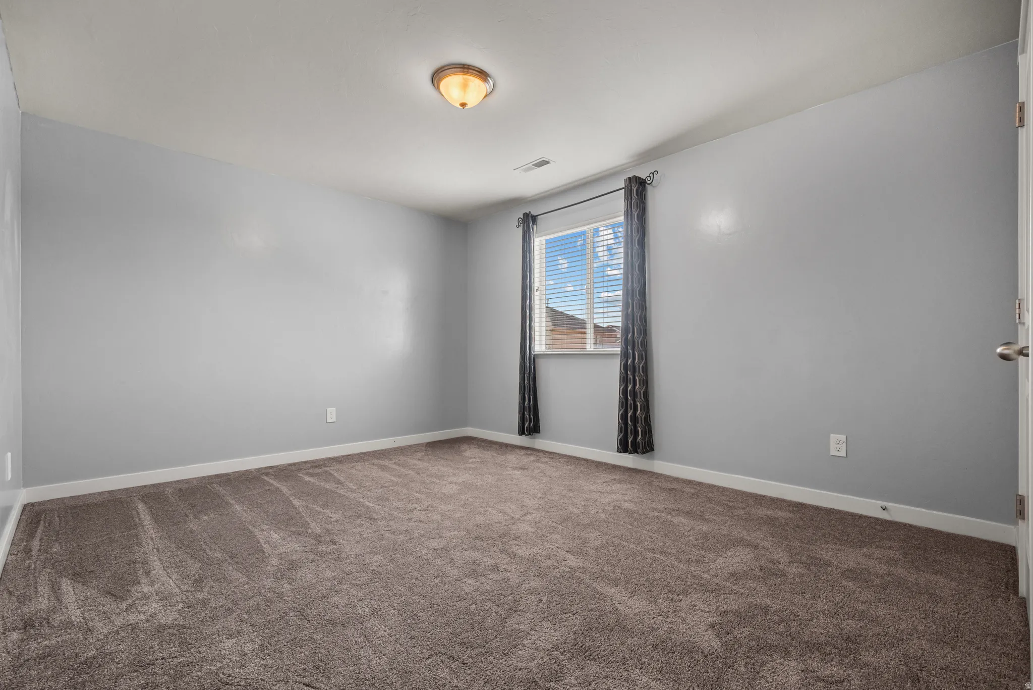Spacious room with plush gray carpeting, light gray wall paint, and white baseboards