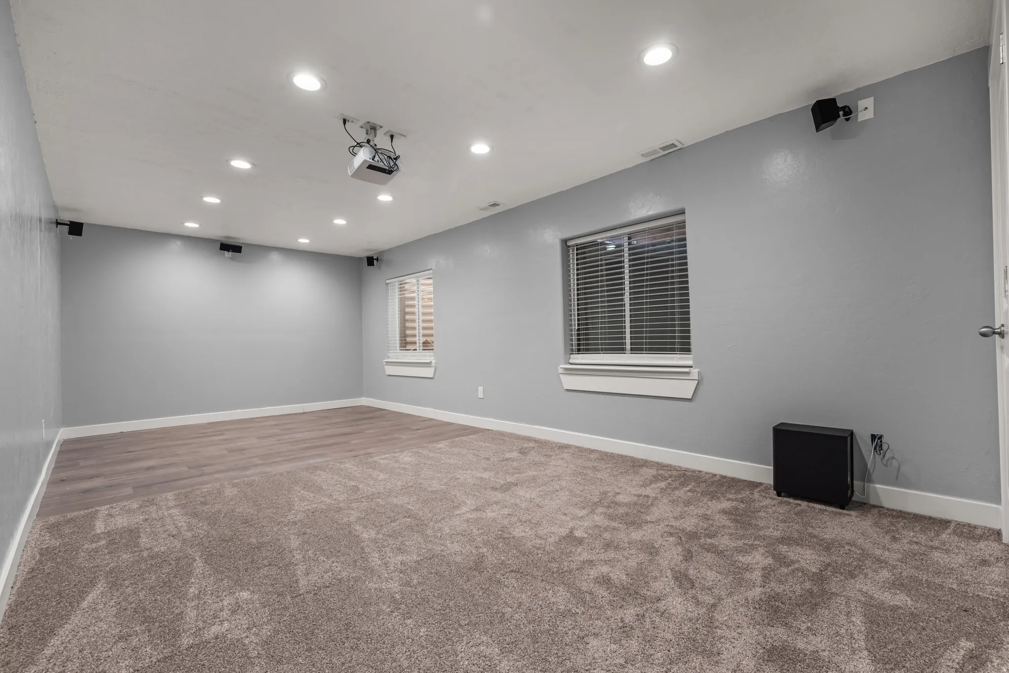 Entertainment room featuring a ceiling-mounted projector, recessed lighting, and wall-mounted speakers