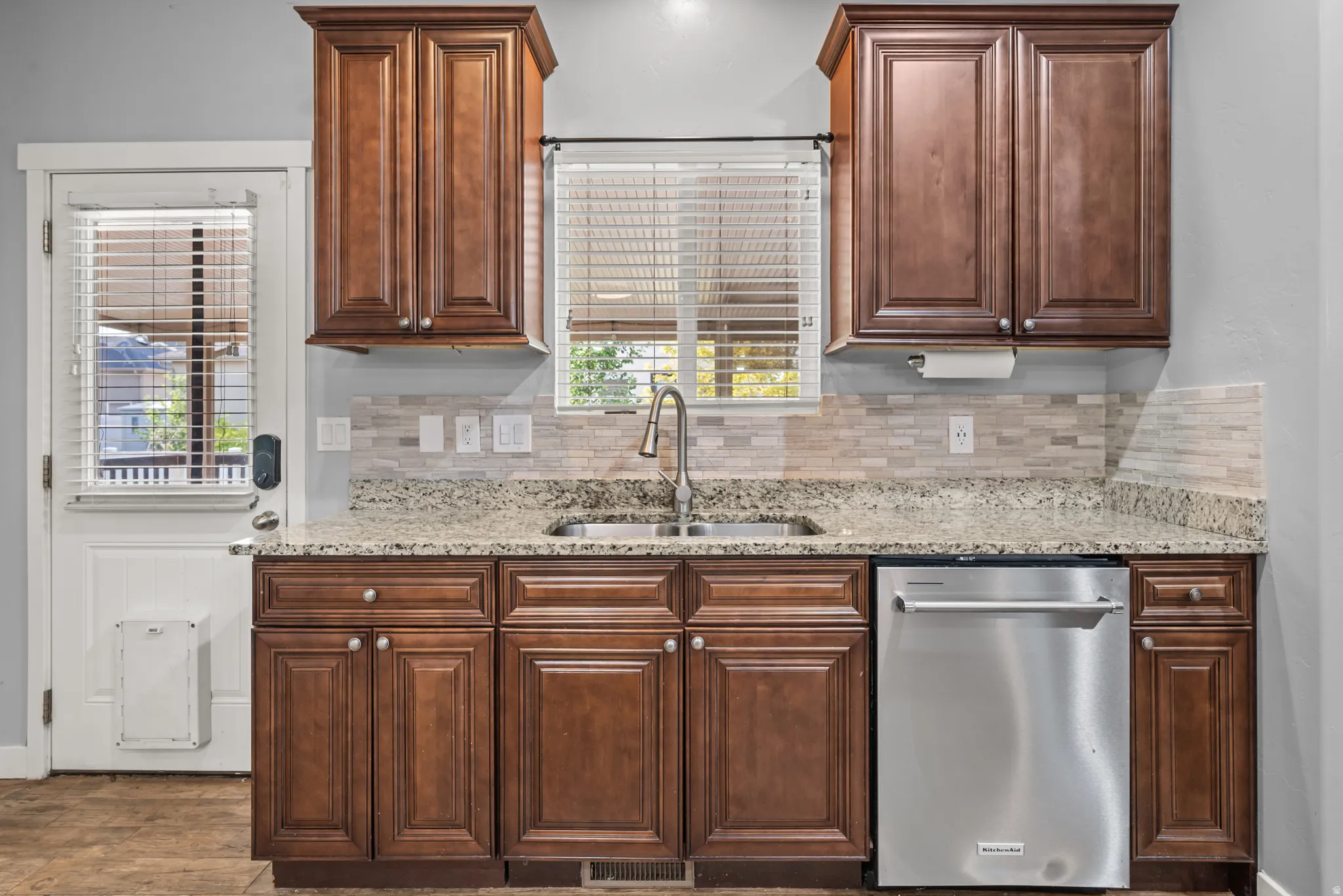 Kitchen sink area featuring a stainless steel double basin sink, granite countertops, tile backsplash, and dark wood cabinetry