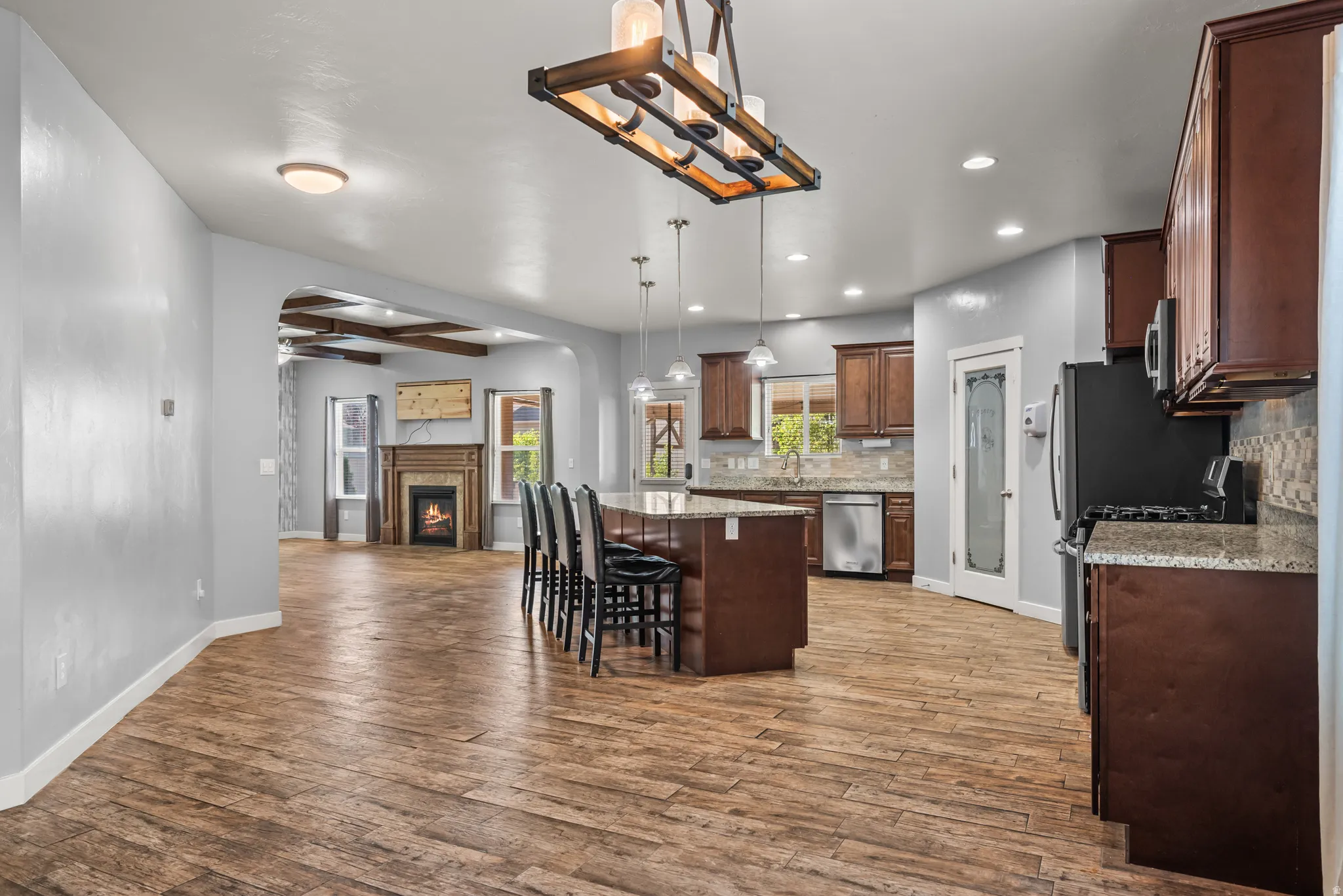 Open-concept living space featuring wood-finish flooring, a kitchen island with seating, dark wood cabinetry, and a fireplace with a mantel