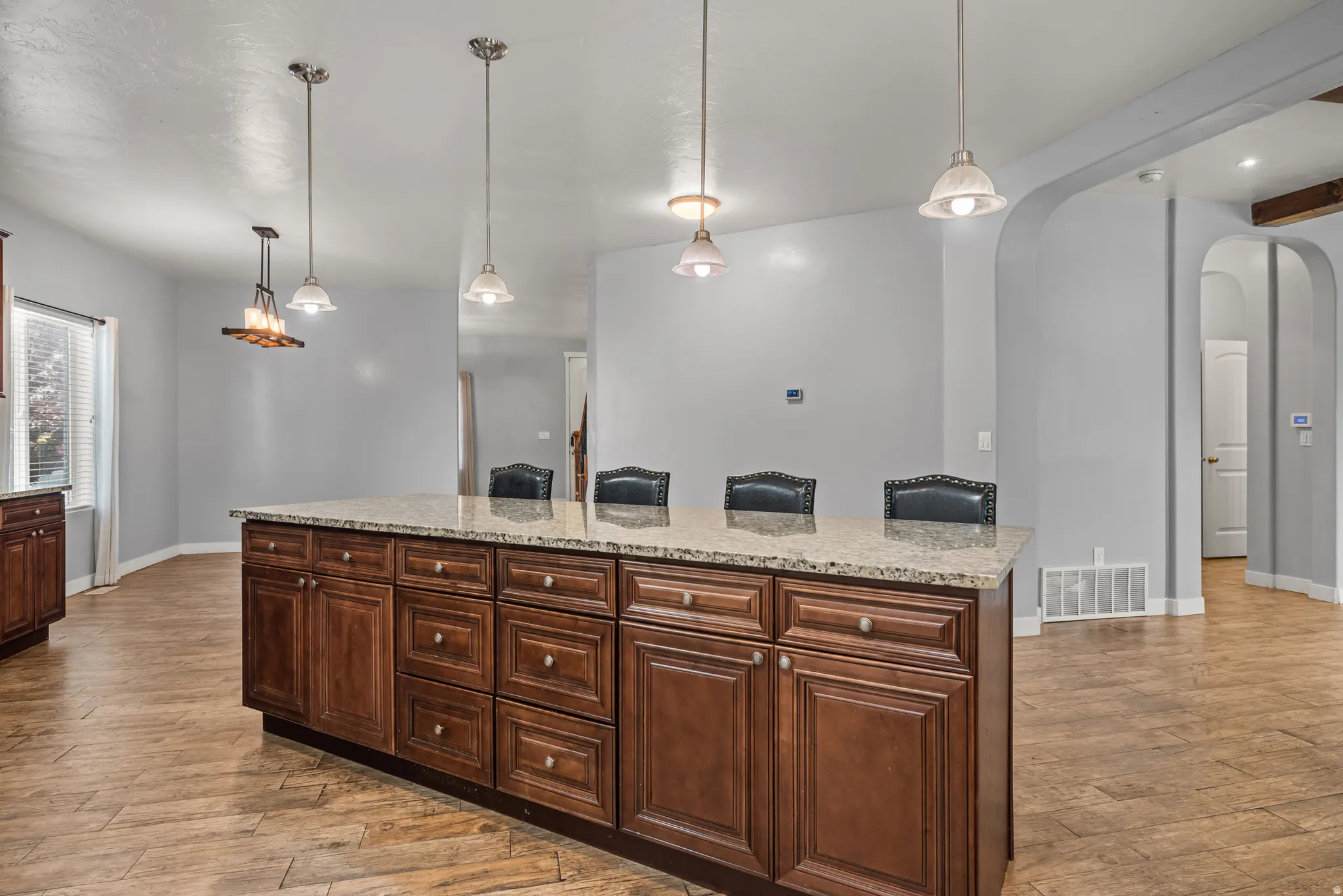 Kitchen island featuring extensive cabinetry with dark wood-finish doors and drawers, a light-toned granite countertop, and integrated seating