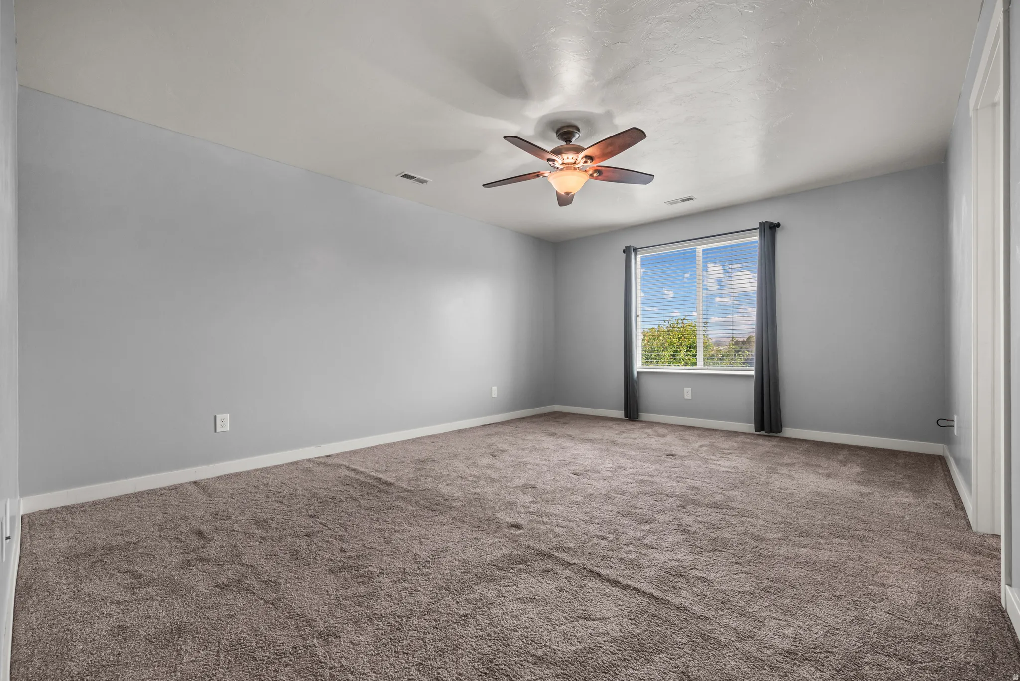 Carpeted room featuring a ceiling fan, light gray walls, white trim, and a window with blinds
