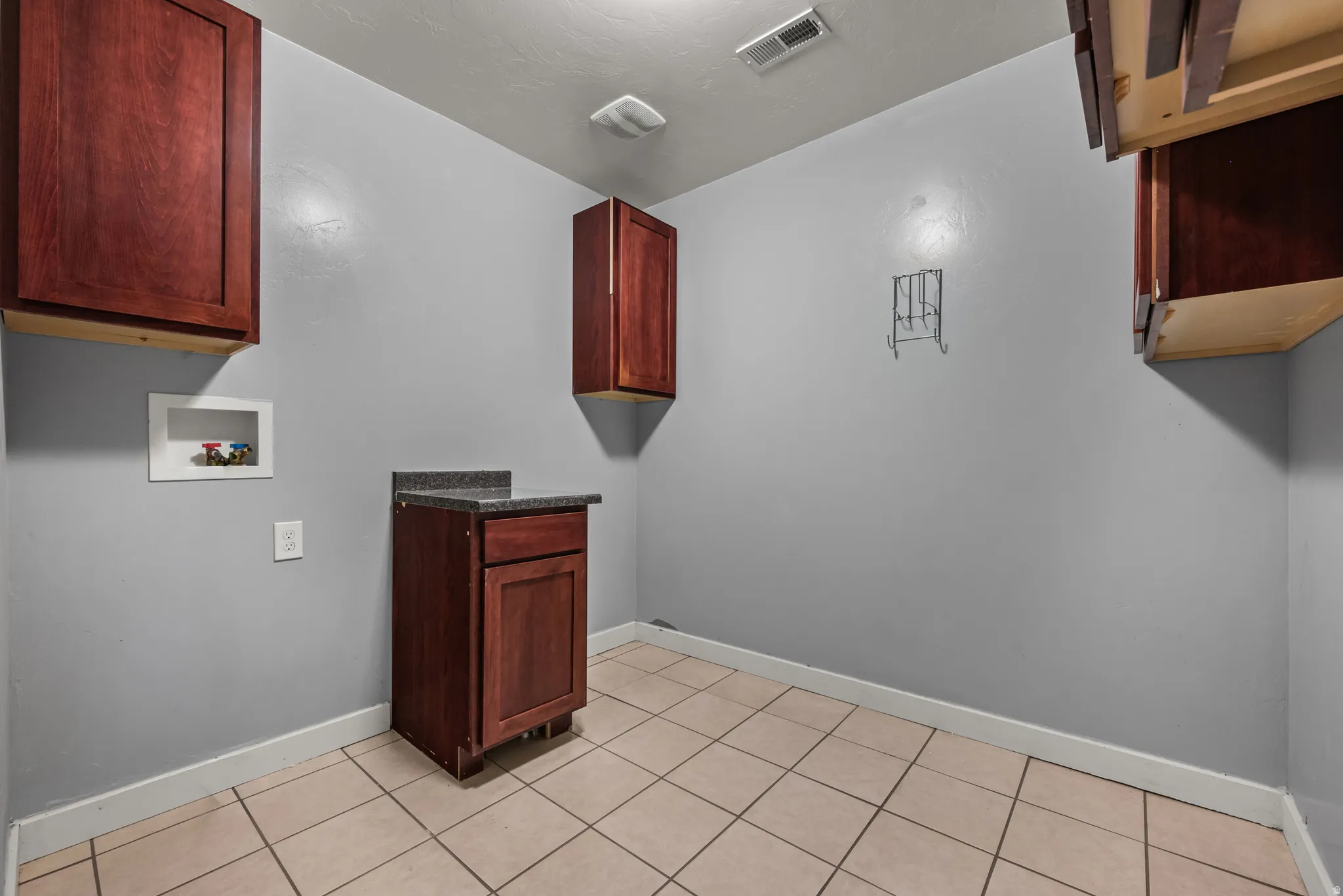 Laundry area featuring tile flooring, a utility sink with a dark countertop, and multiple wall-mounted wood-finish cabinets