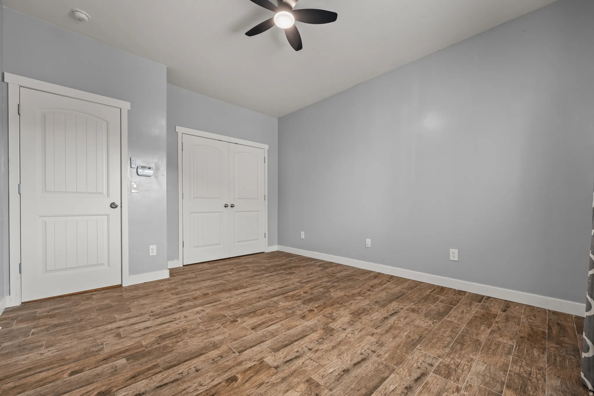 Spacious room featuring wood-finish flooring, light gray walls, white trim, and a ceiling fan