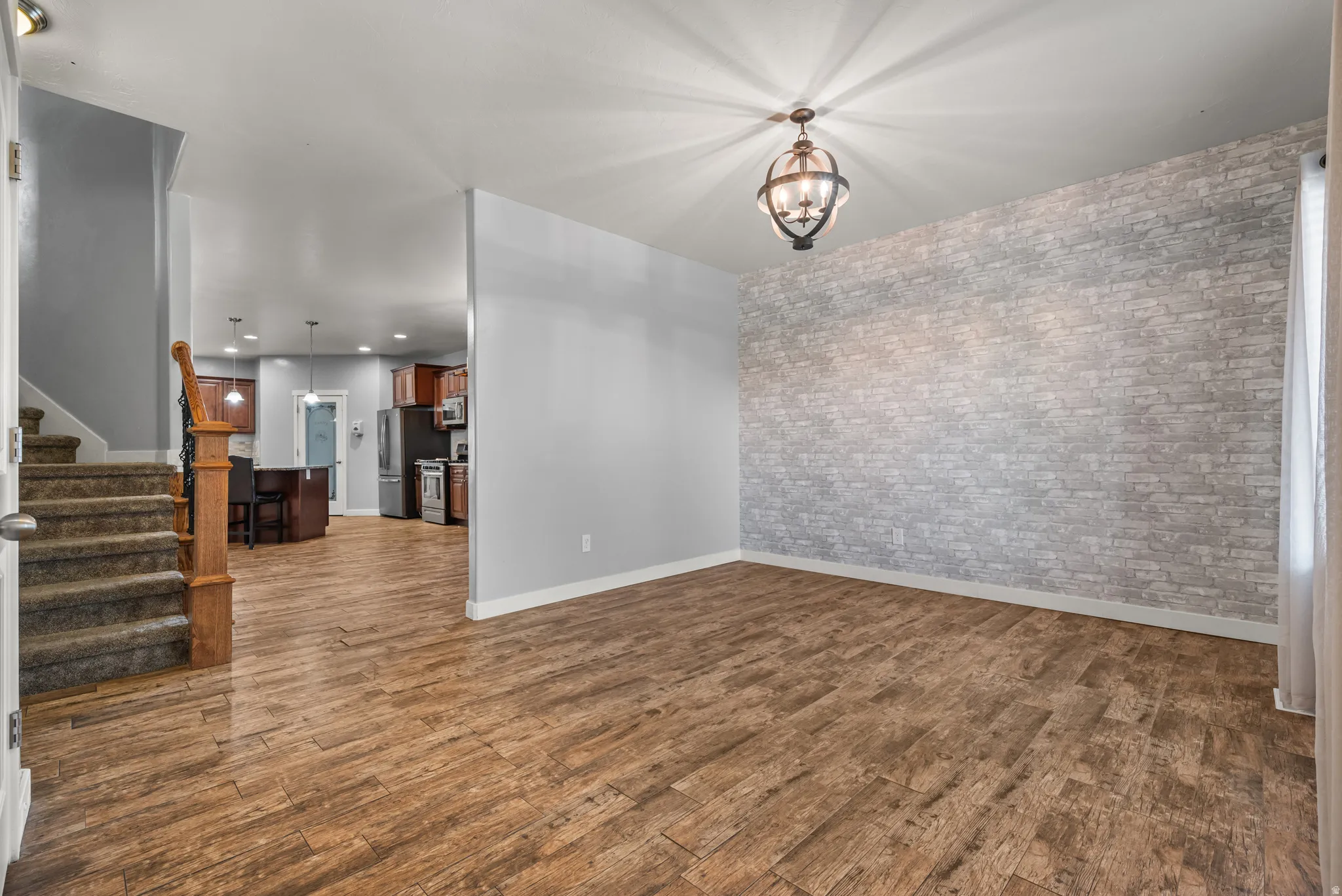 Spacious interior featuring wood-finish flooring, a decorative brick accent wall, and an orb chandelier