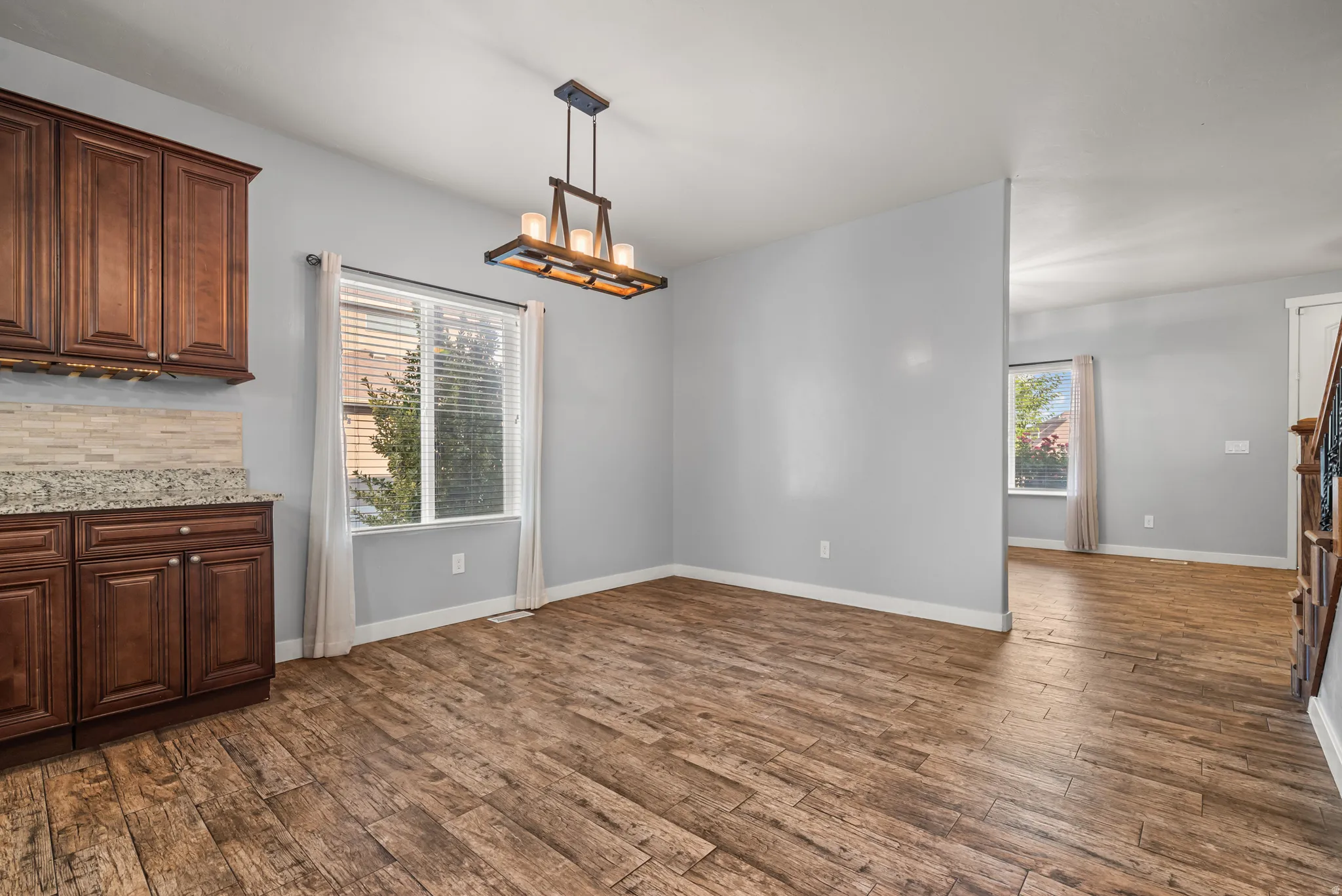 Open-concept space featuring wood-finish flooring, a modern linear chandelier, and a built-in cabinetry unit with granite-style countertops and a neutral tile backsplash
