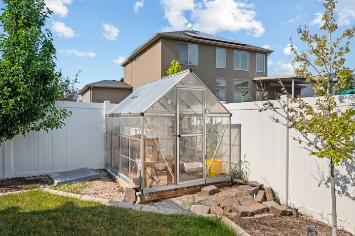Rear yard featuring a clear-paneled greenhouse with a pitched roof, a white vinyl privacy fence, and mature trees