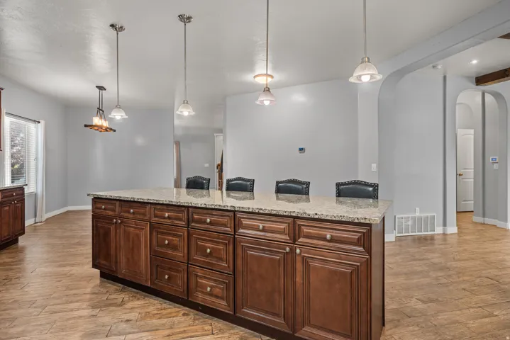 Kitchen island featuring extensive cabinetry with dark wood-finish doors and drawers, a light-toned granite countertop, and integrated seating