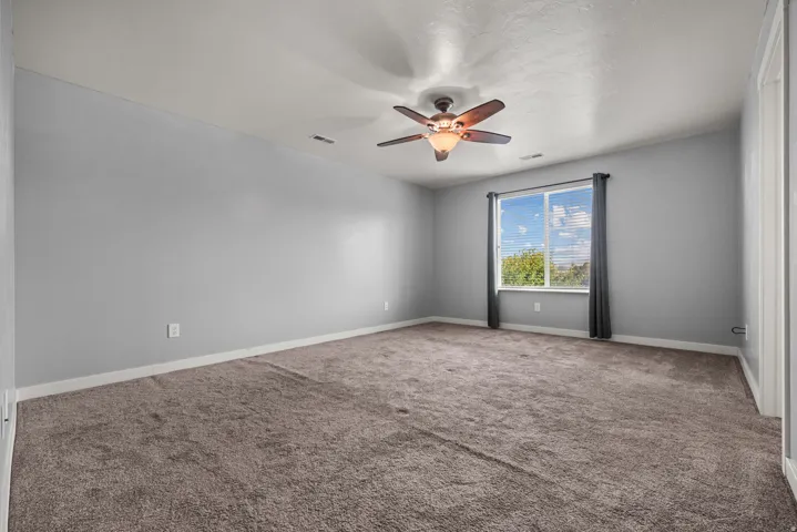 Carpeted room featuring a ceiling fan, light gray walls, white trim, and a window with blinds