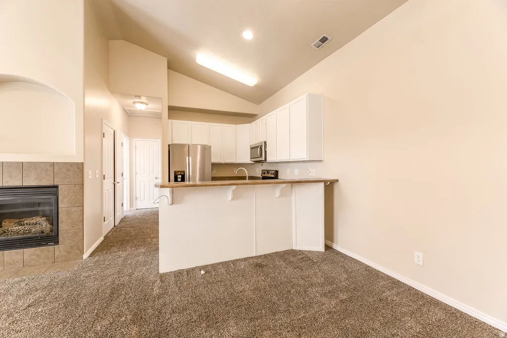 Open-concept living space featuring a fireplace with tile surround, vaulted ceilings, and plush carpeting