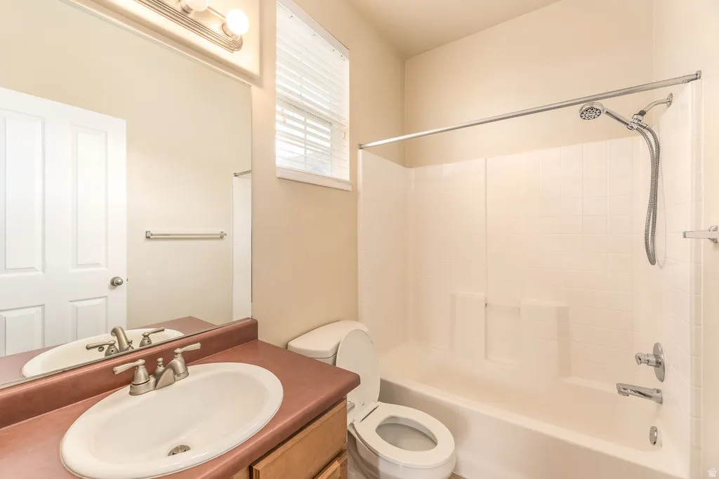 Bathroom featuring a shower-over-tub combination with white tile surround, a single vanity with an oval basin, and a toilet
