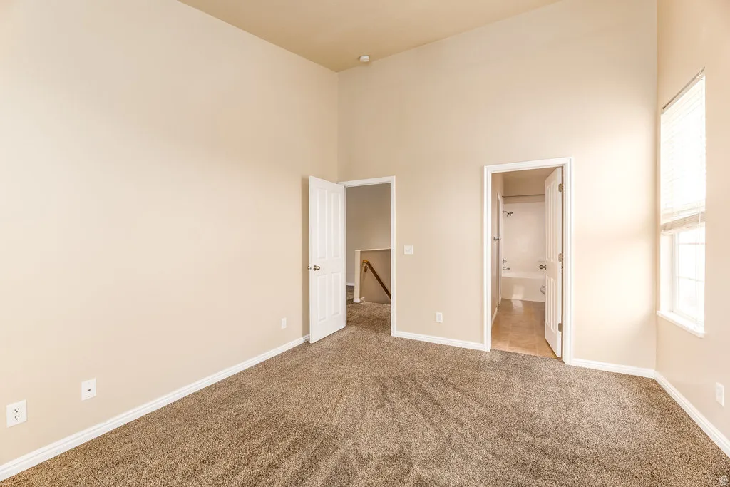 Carpeted room featuring a high ceiling, neutral wall paint, white trim, and a window with blinds