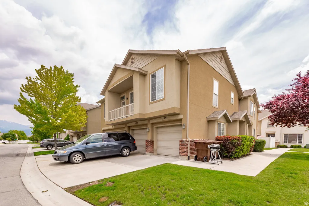 Multi-level stucco exterior featuring an upper balcony with white railing, a two-car garage, and a brick veneer accent