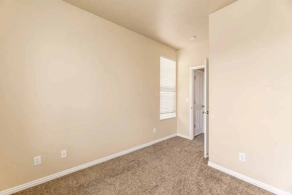 Carpeted room featuring a window with horizontal blinds, light beige walls, and white baseboards