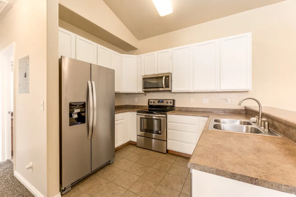 Kitchen featuring white cabinetry, stainless steel appliances, a double basin sink, and tile flooring