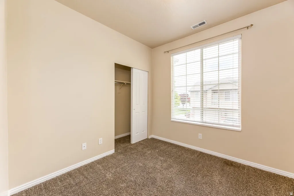 Neutral-toned room featuring a large window with horizontal blinds, plush carpeting, and a built-in closet with bi-fold doors