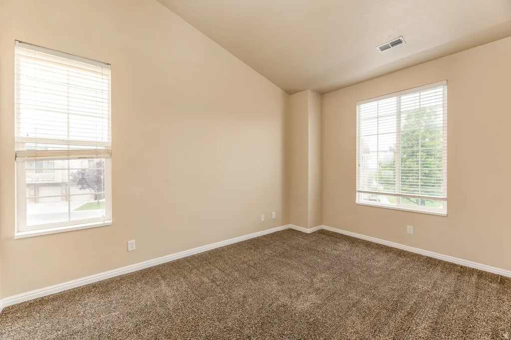 Vaulted ceiling room featuring two large windows with blinds, neutral wall tones, and plush carpet flooring