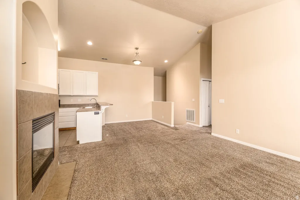 Open-concept living area featuring a tile-surround fireplace, vaulted ceilings, recessed lighting, and a kitchen with white cabinetry and a breakfast bar