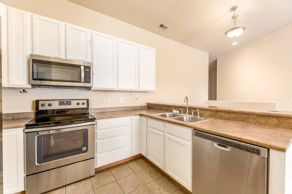 Kitchen featuring white cabinetry, stainless steel appliances, a dual basin sink, and tile flooring