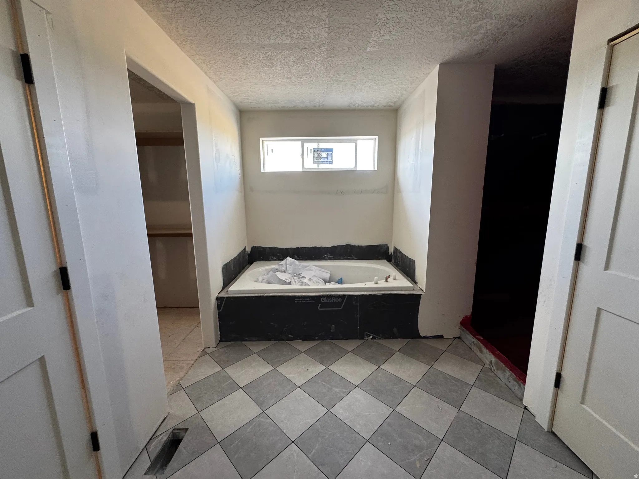 Spacious bathroom featuring a built-in soaking tub with black tile surround, checkerboard tile flooring, and a horizontal window