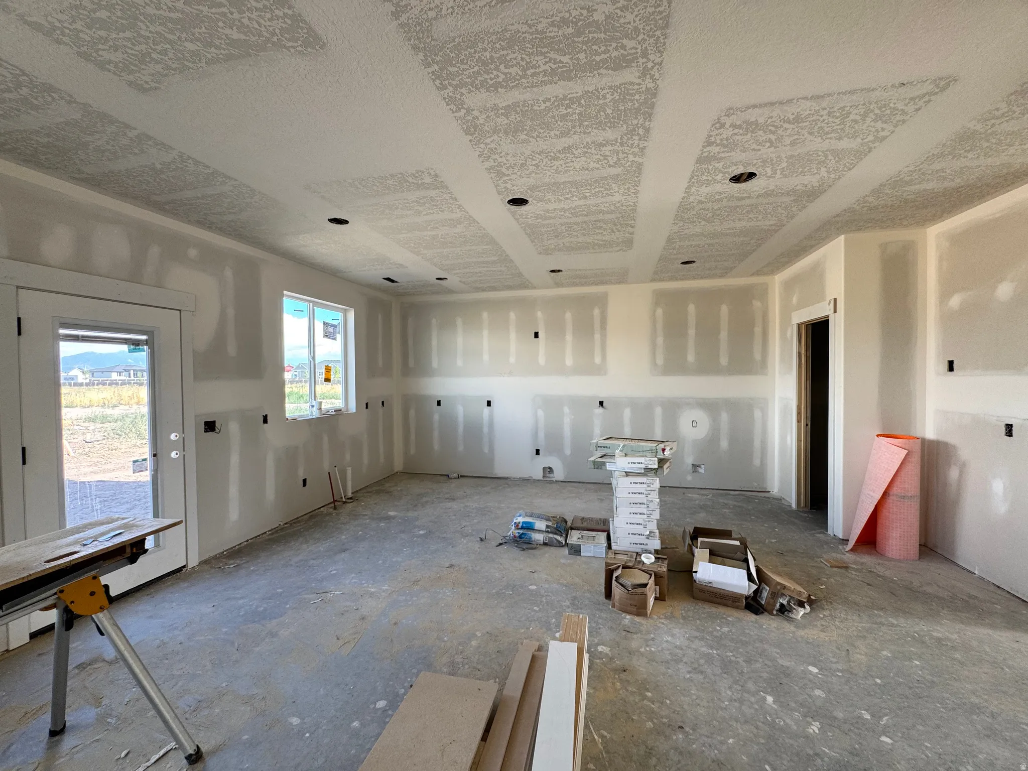 Unfinished interior space featuring drywall installation, recessed lighting, a back door with glass, and a large window