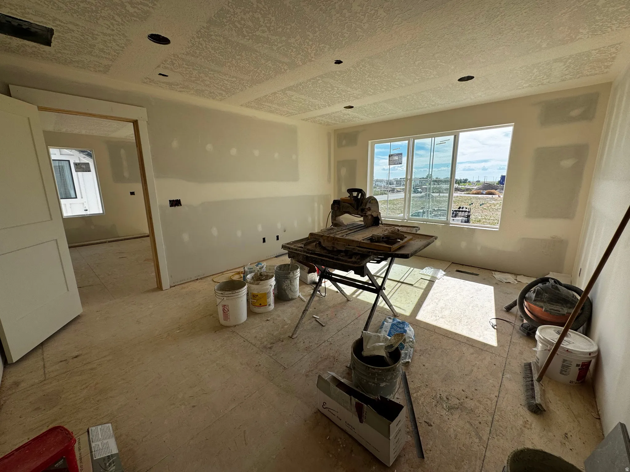 Interior space under construction featuring a three-pane window, recessed lighting, and an open doorway to an additional room