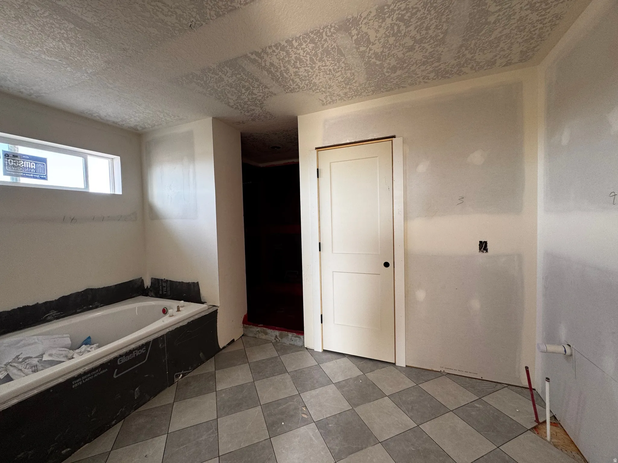 Bathroom under construction featuring a built-in tub, horizontally oriented window, and a white two-panel door with black hardware