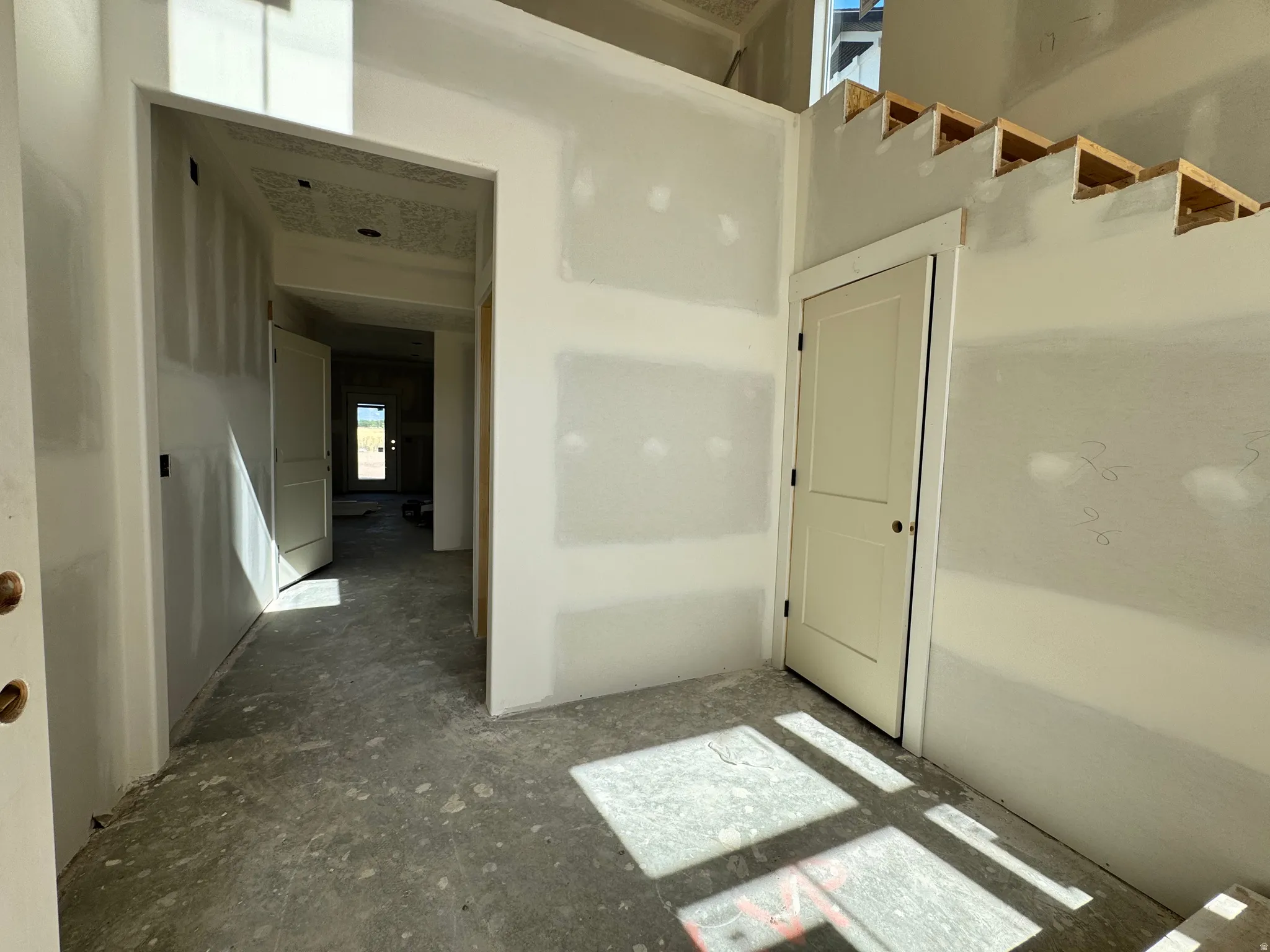 Interior featuring unfinished walls, a solid core door with black hardware, and an exposed stair framing